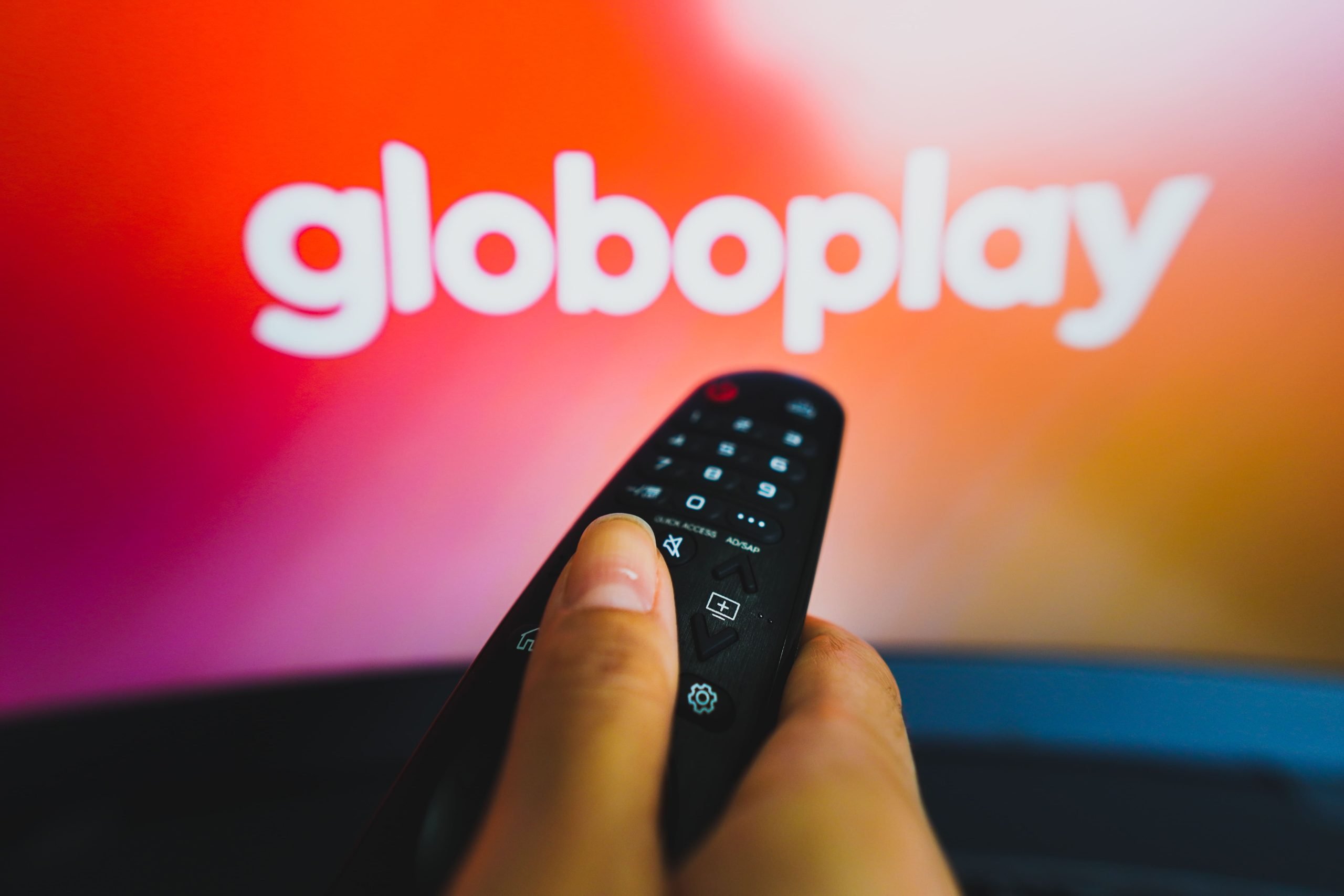 Televisão ao fundo com um controle remoto apontando para iniciar um dos melhores filmes do Globoplay