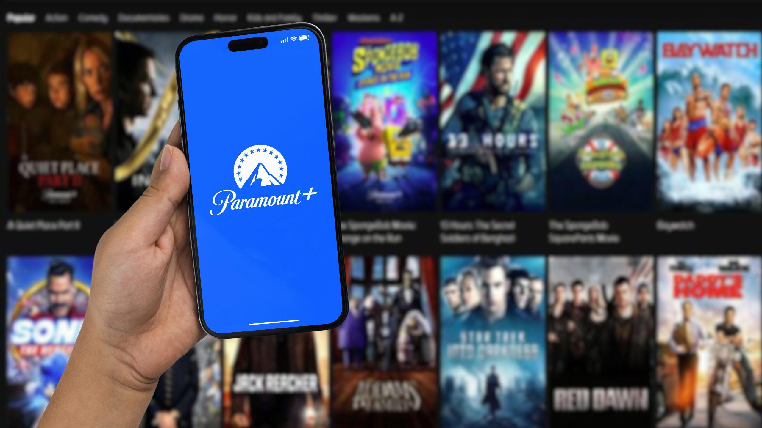 Fundo com vários filmes e séries e um celular pronto para começar a ver os melhores filmes da Paramount