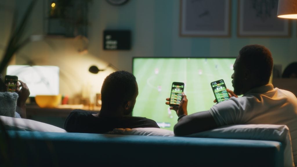 homens assistindo a jogo na tv e com celular no aplicativo