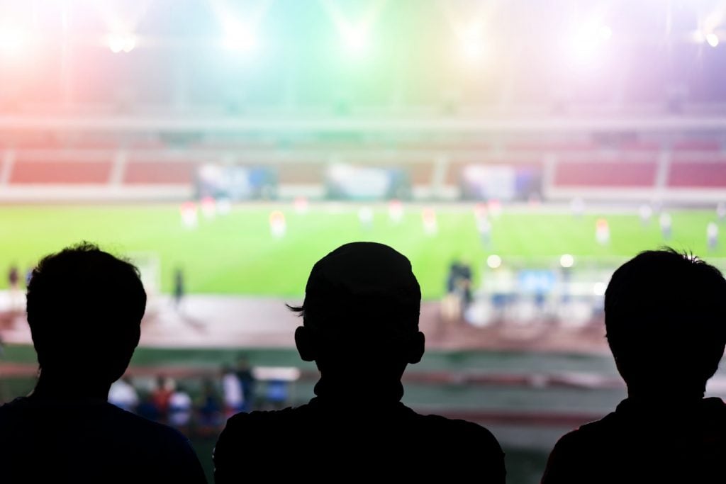 Três jovens em um estádio de futebol assistindo ao jogo