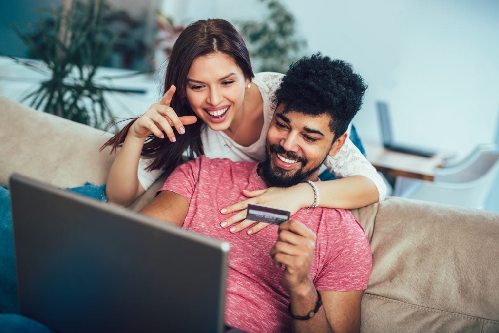 homem e mulher sorrindo com cartão na mão e notebook