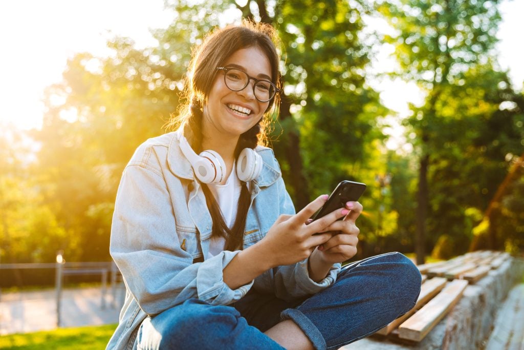 moça de óculos sorrindo e com celular na mão e fone de ouvido